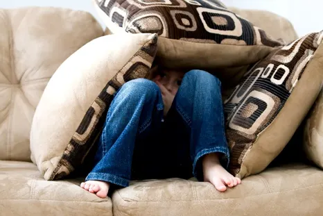 child hiding under pillows