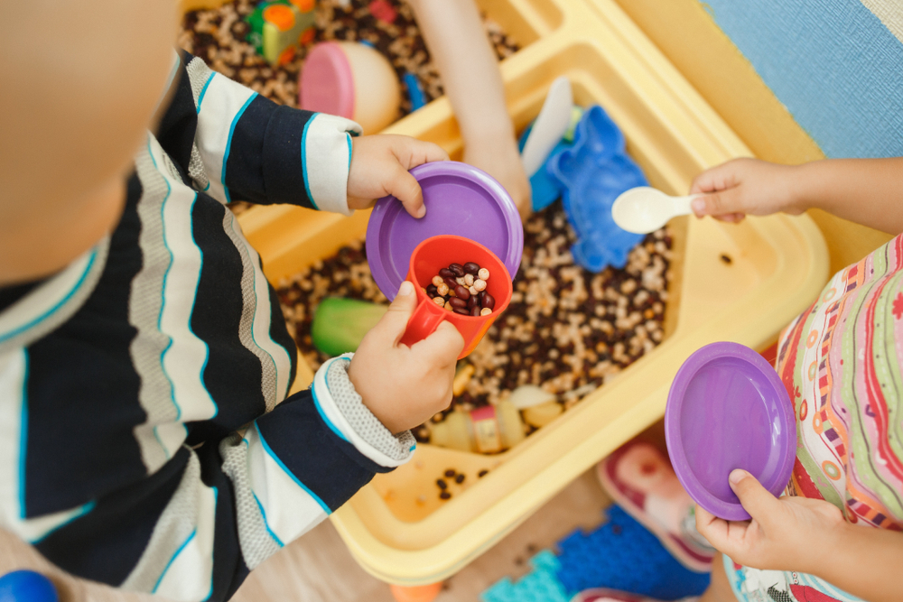 image of children playing in bean filled sensory bin with plastic dishes.