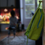 image of backpack hanging on door while child watches TV. Parents looking for screen free after school activities for their child.