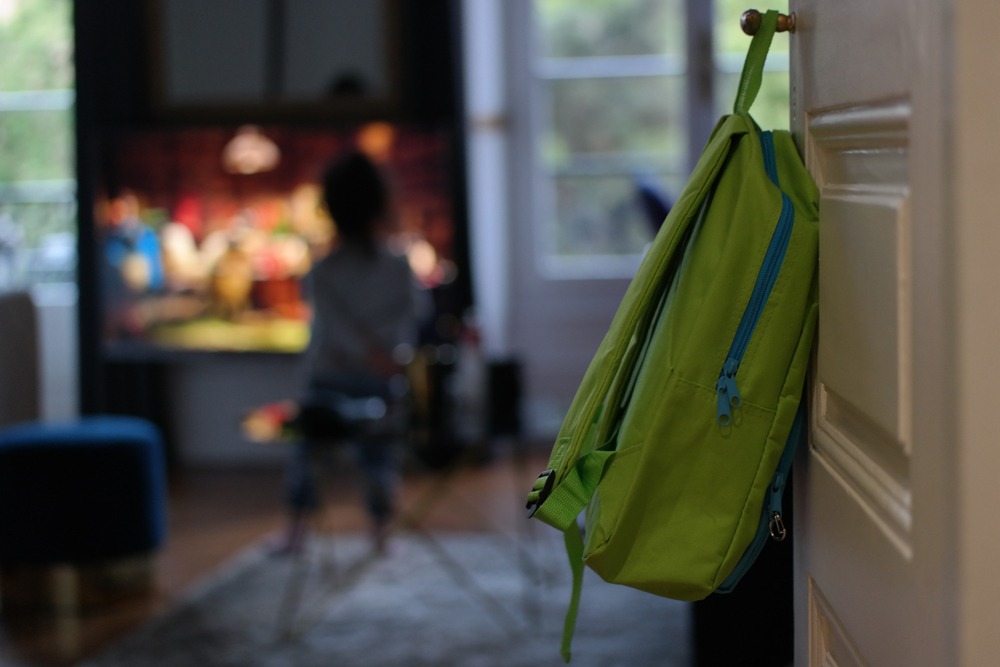 image of backpack hanging on door while child watches TV. Parents looking for screen free after school activities for their child.