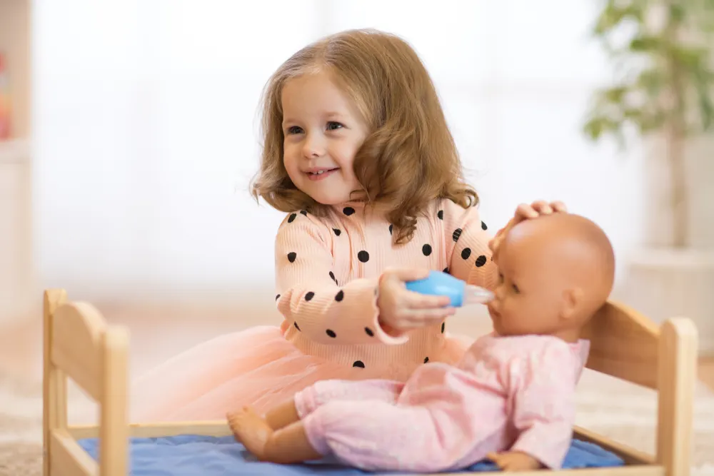 image of toddler taking care of baby doll while mother nurses newborn.