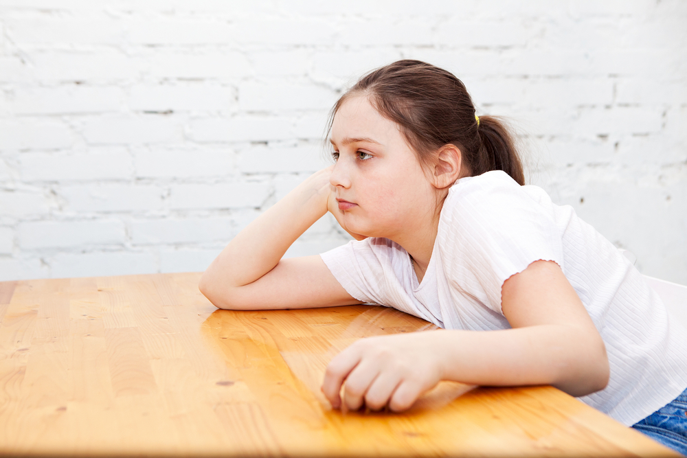 image of 10 year old with elbow on a table, looking bored. In need of screen free activities for 10 year olds.