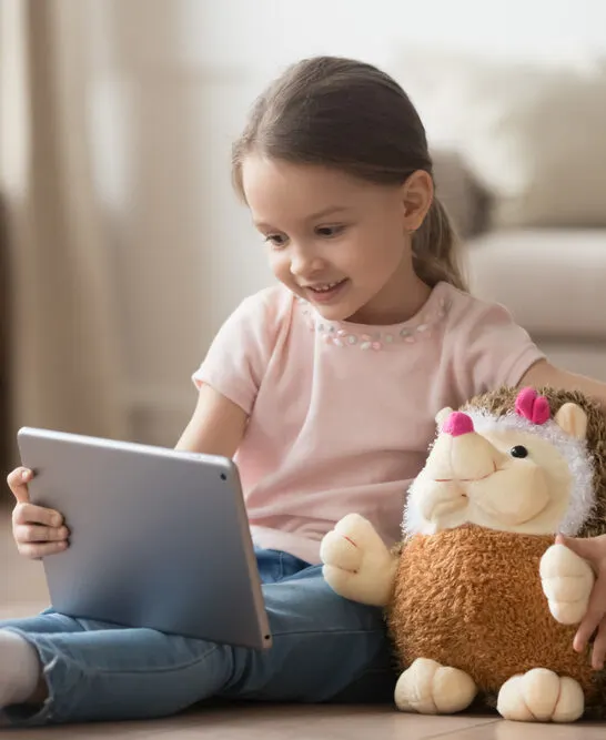 Image of child holding stuffy and watching a tablet. Parent wondering does Ms. Rachel count as screen time.