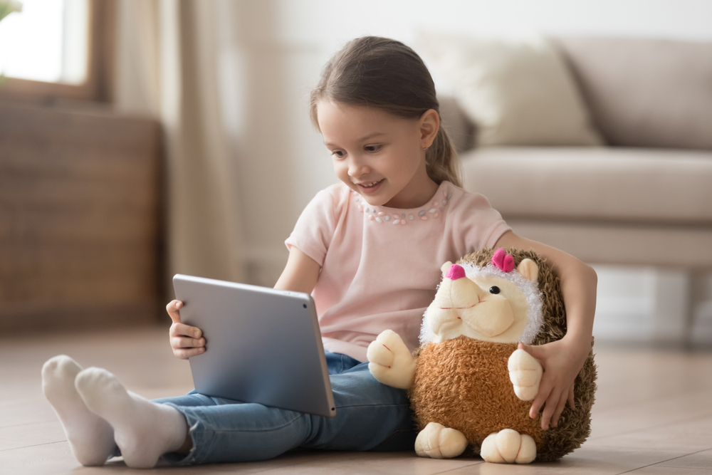 Image of child holding stuffy and watching a tablet. Parent wondering does Ms. Rachel count as screen time.